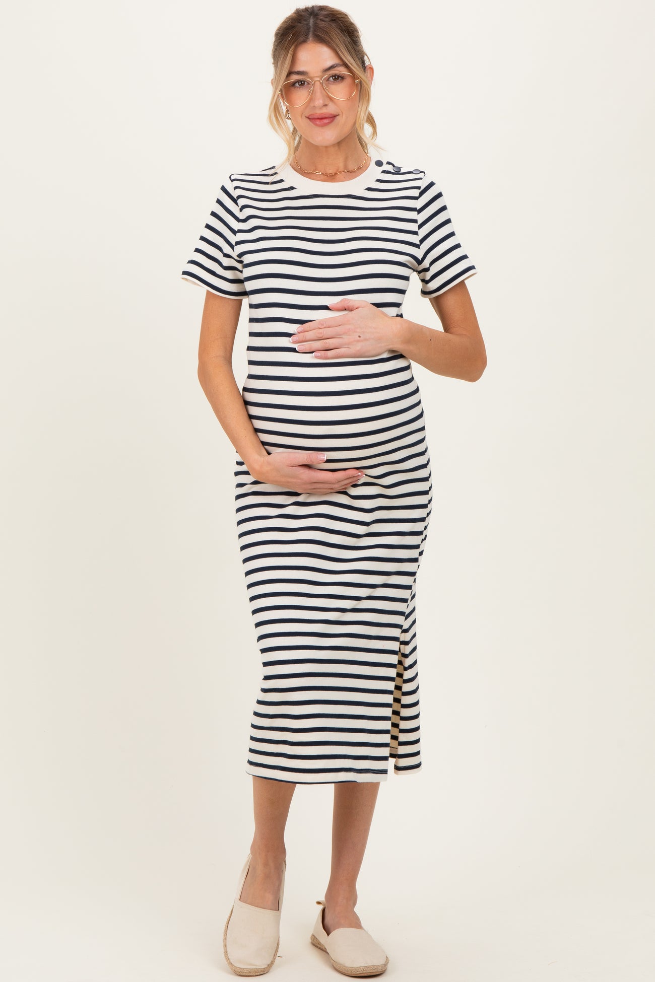 woman wearing a navy and white striped maternity dress with a side slit and holding her baby bump