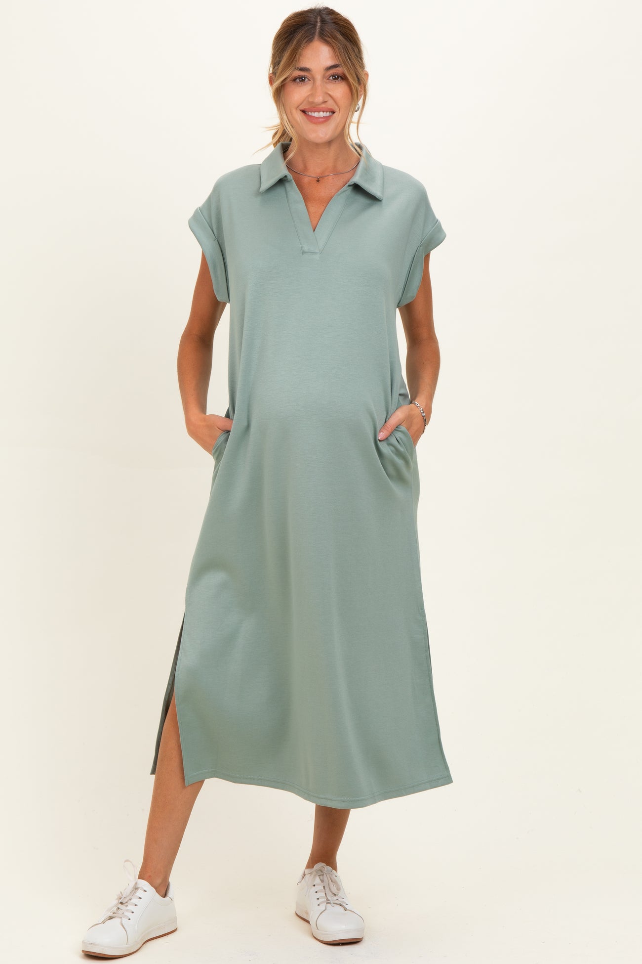 woman wearing a sage green maternity dress with a collared neckline and side pockets, featuring a relaxed fit and slit details