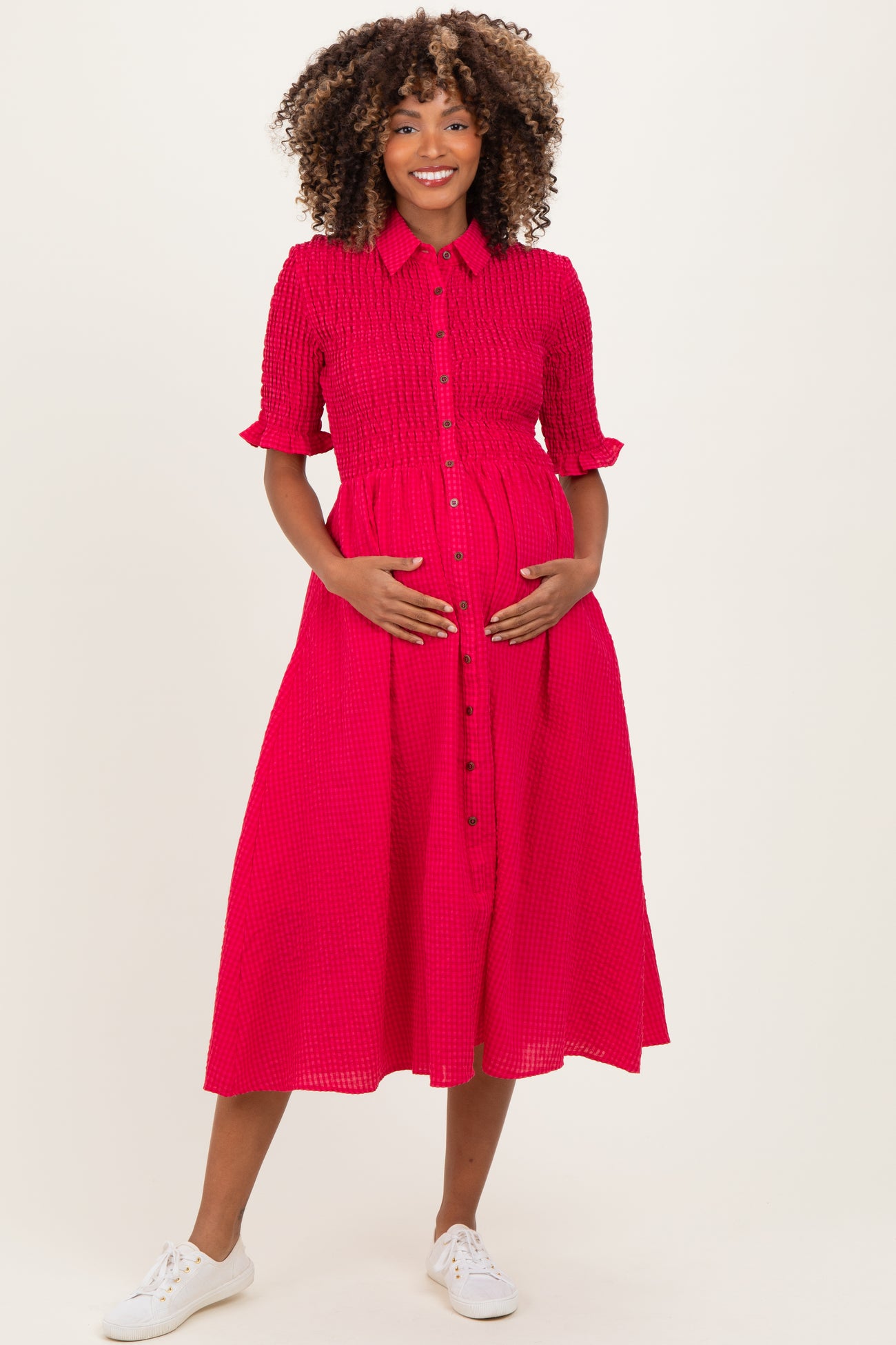 woman wearing a bright pink maternity dress with a button-down front and a belted waist, showing her baby bump