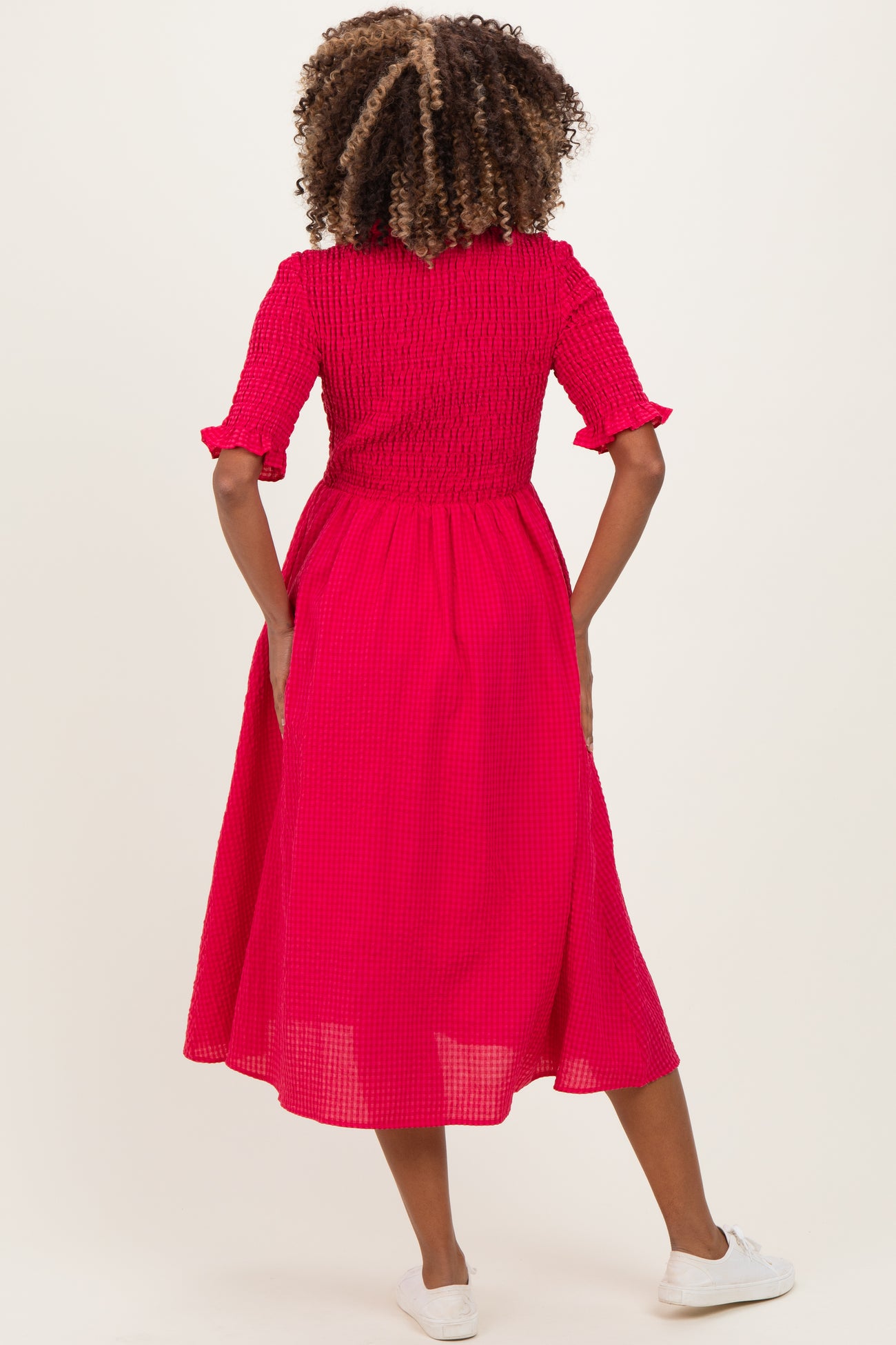woman wearing a bright pink maternity dress with a smocked bodice and short sleeves, shown from the back