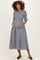 woman wearing a black and white checkered maternity dress with puff sleeves and a smocked bodice, holding her baby bump