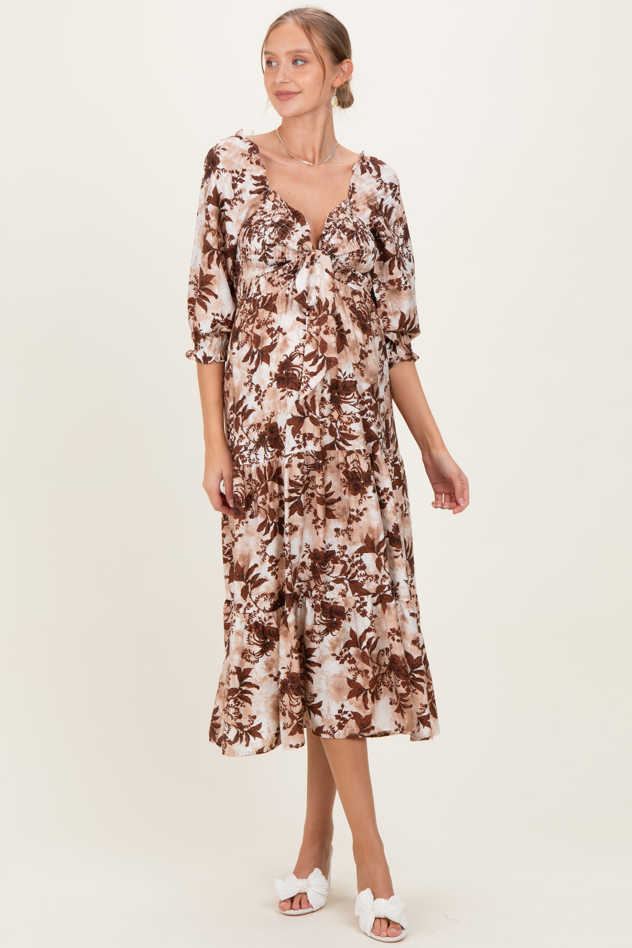 woman wearing a brown floral print maternity dress with a tie front and elbow-length sleeves, showing her baby bump