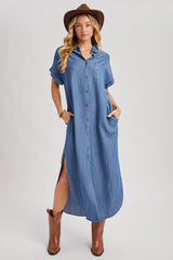 woman wearing a light blue denim maxi shirt dress with short sleeves and side pockets, paired with a brown hat and tall boots