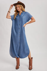 woman wearing a blue denim shirt dress with short sleeves and a front pocket, styled with brown cowboy boots and a hat