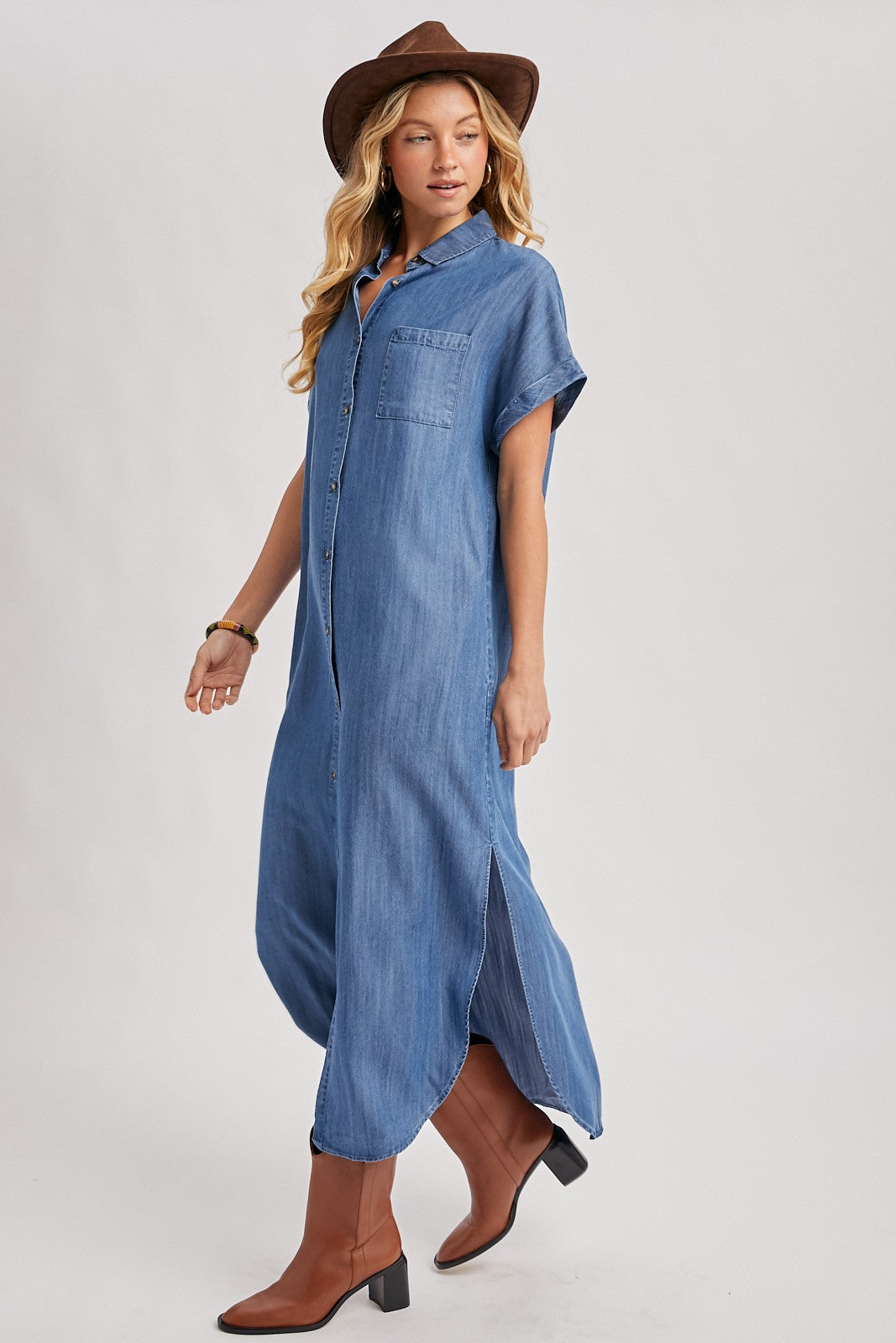 woman wearing a blue denim button-up maxi dress and a brown hat, paired with brown knee-high boots