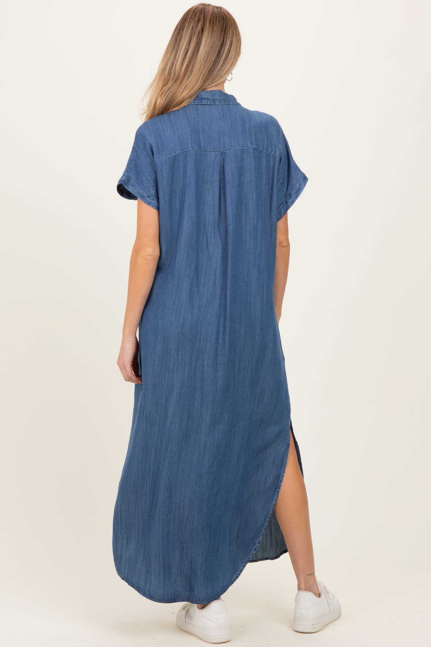 woman wearing a denim maternity maxi dress with short sleeves and a high slit, showcasing a baby bump