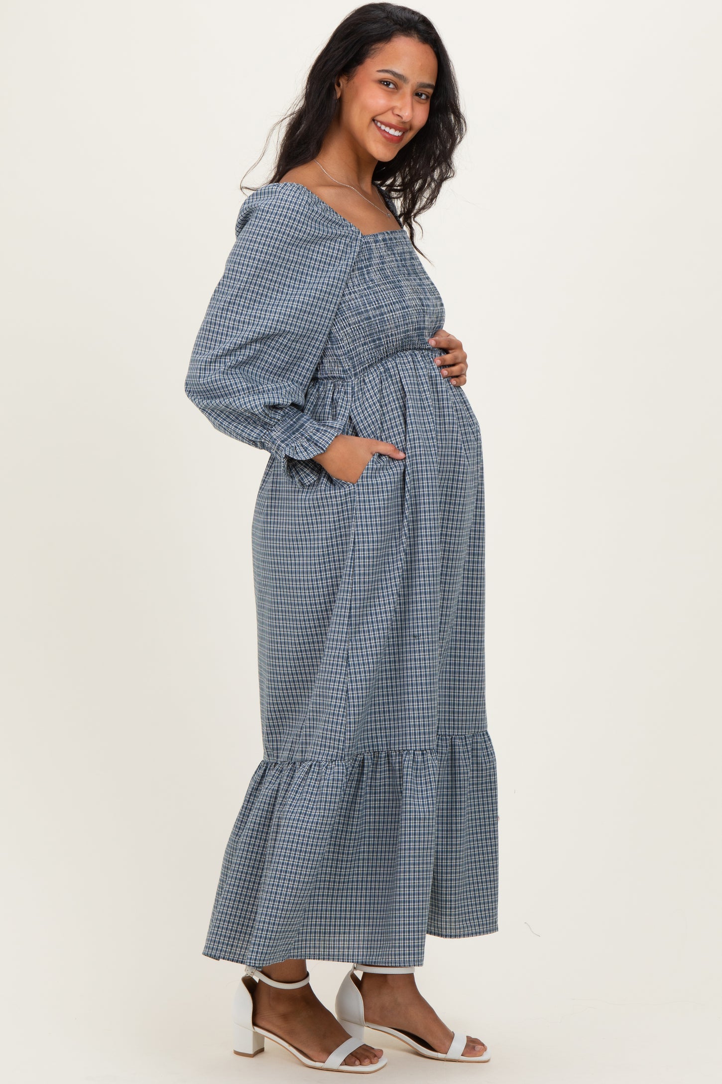 woman wearing a blue and white checkered maternity dress with a tiered hem and pockets, showing her baby bump