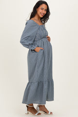 woman wearing a blue and white checkered maternity dress with a tiered hem and pockets, showing her baby bump