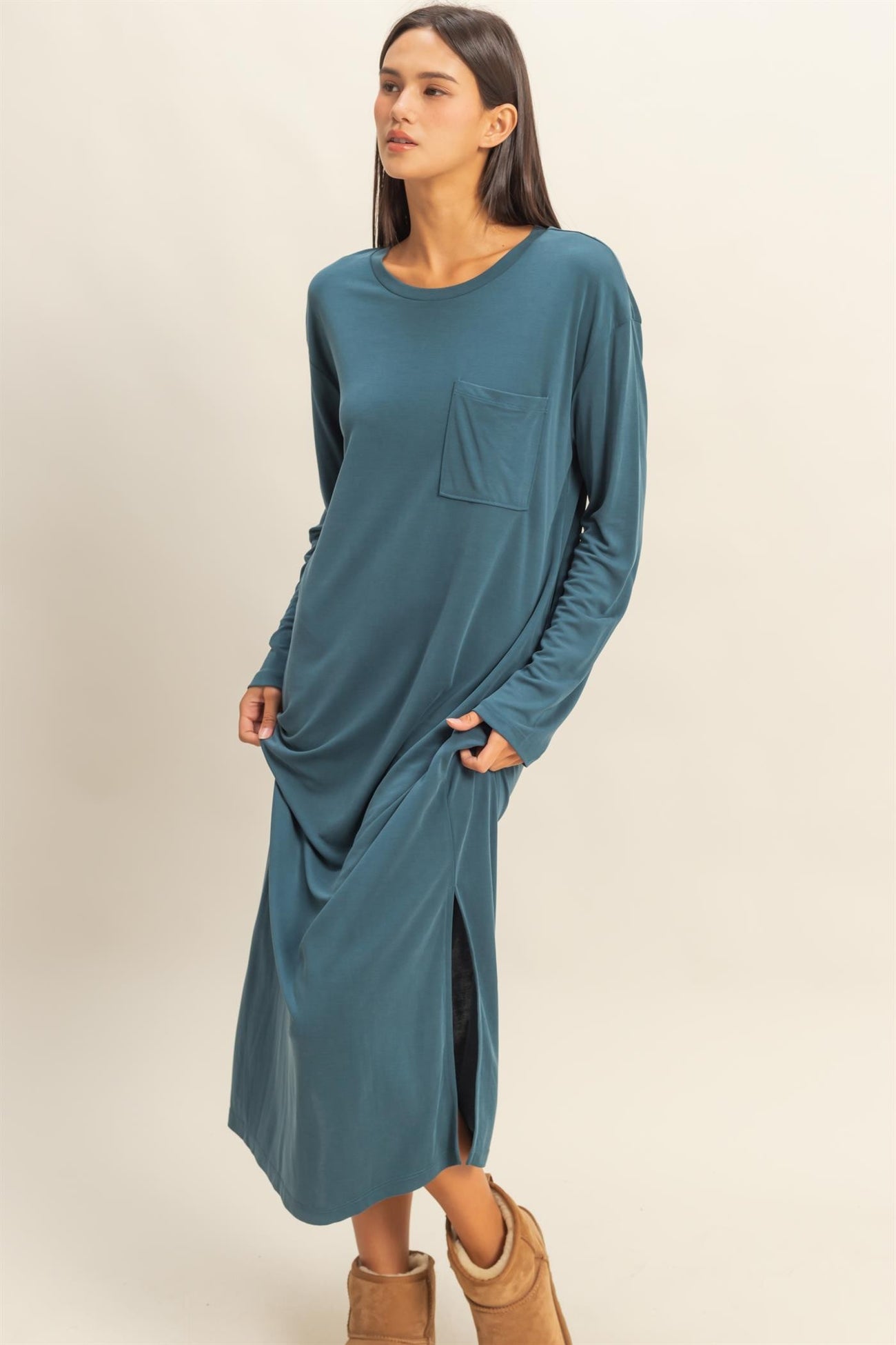 woman wearing a teal long sleeve maxi dress with a pocket and side slits, standing with hands in pockets