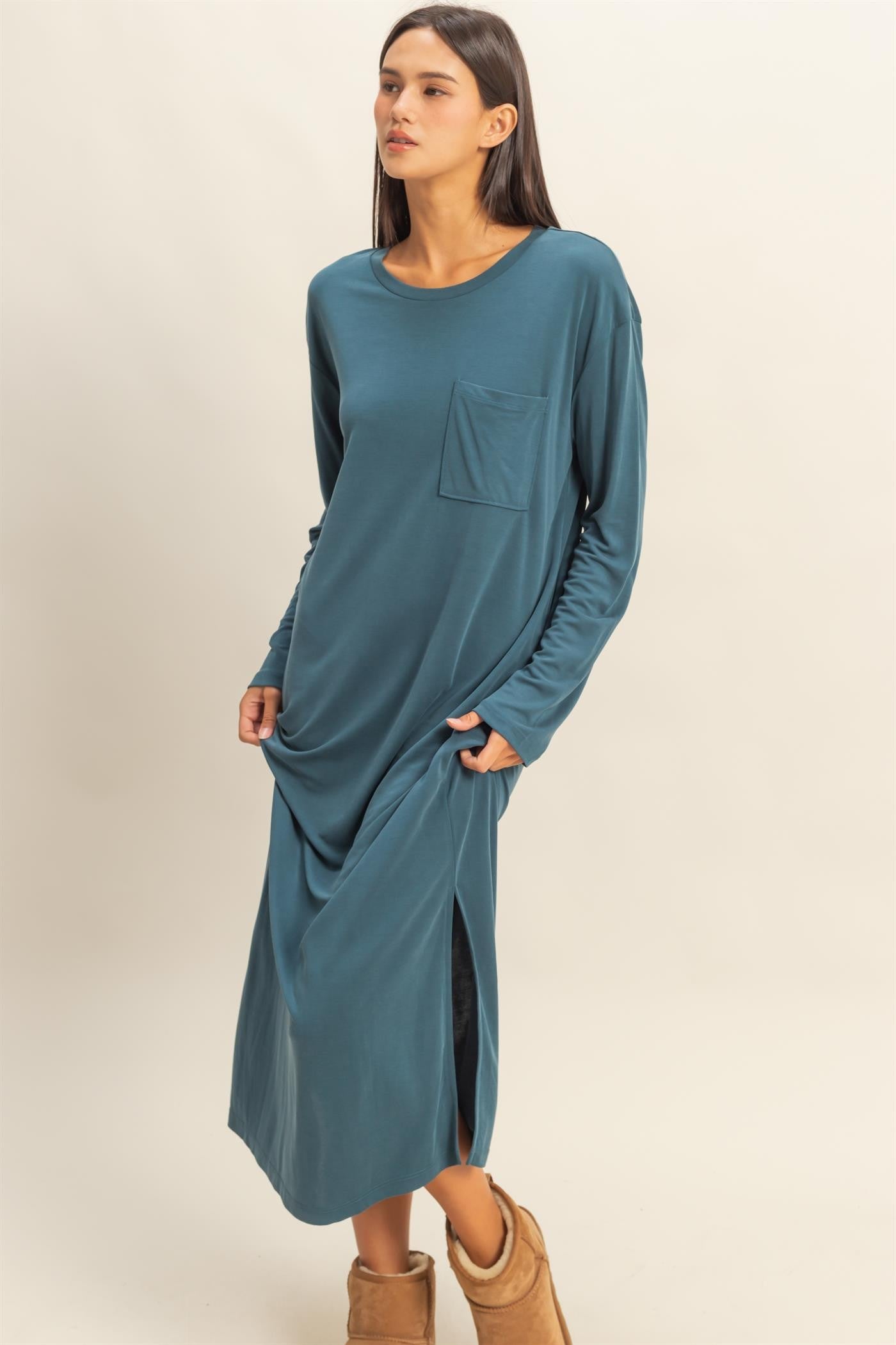 woman wearing a teal long sleeve maxi dress with a pocket and side slits, standing with hands in pockets