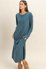 woman wearing a teal long sleeve maxi dress with a pocket and side slits, standing with hands in pockets