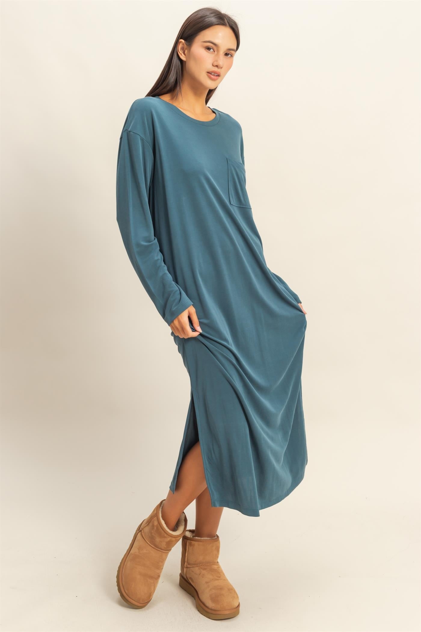 woman wearing a teal long sleeve maxi dress with side slits and a front pocket, paired with tan ankle boots