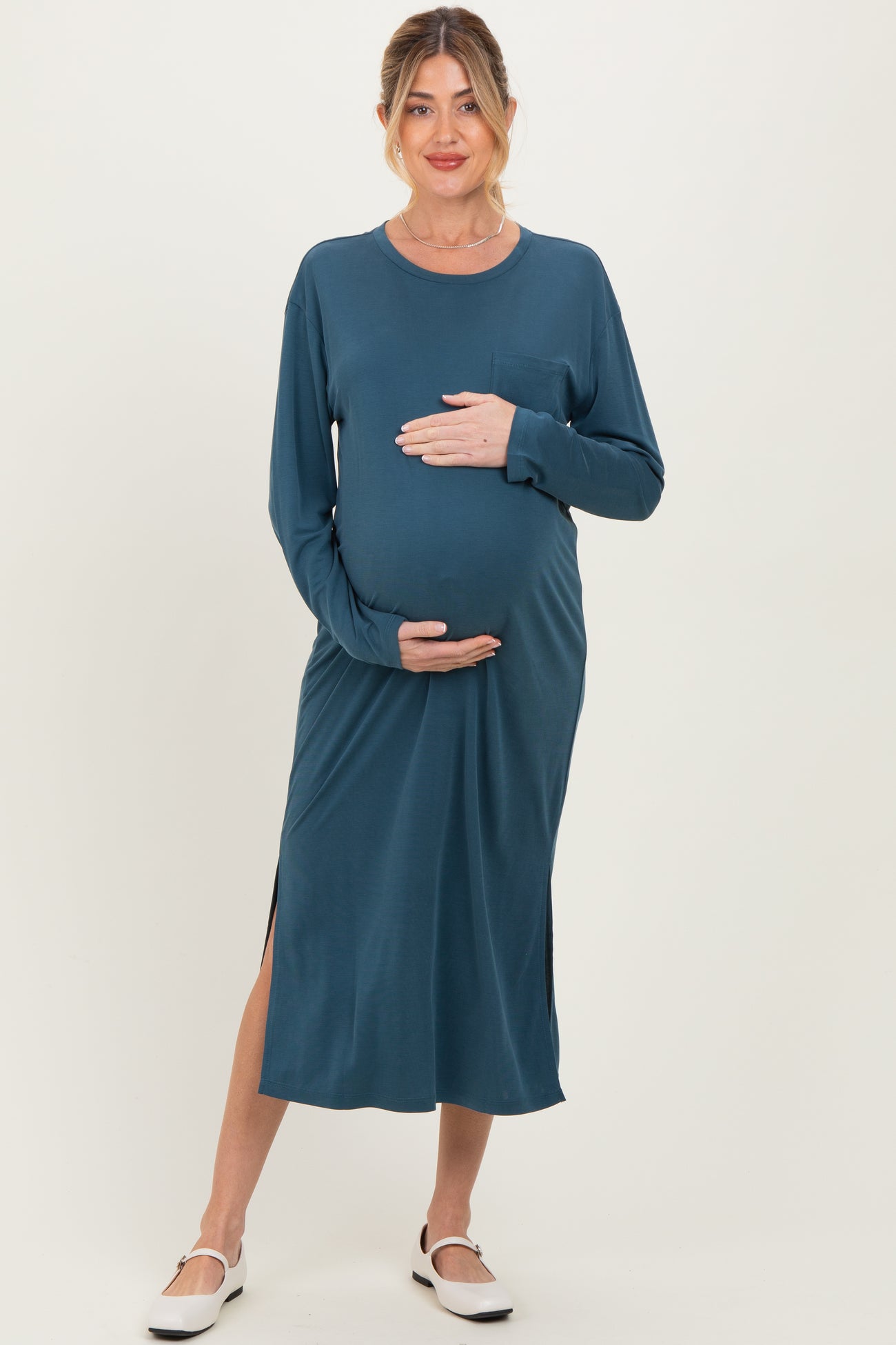 woman wearing a teal long sleeve maternity dress with a side slit and holding her baby bump