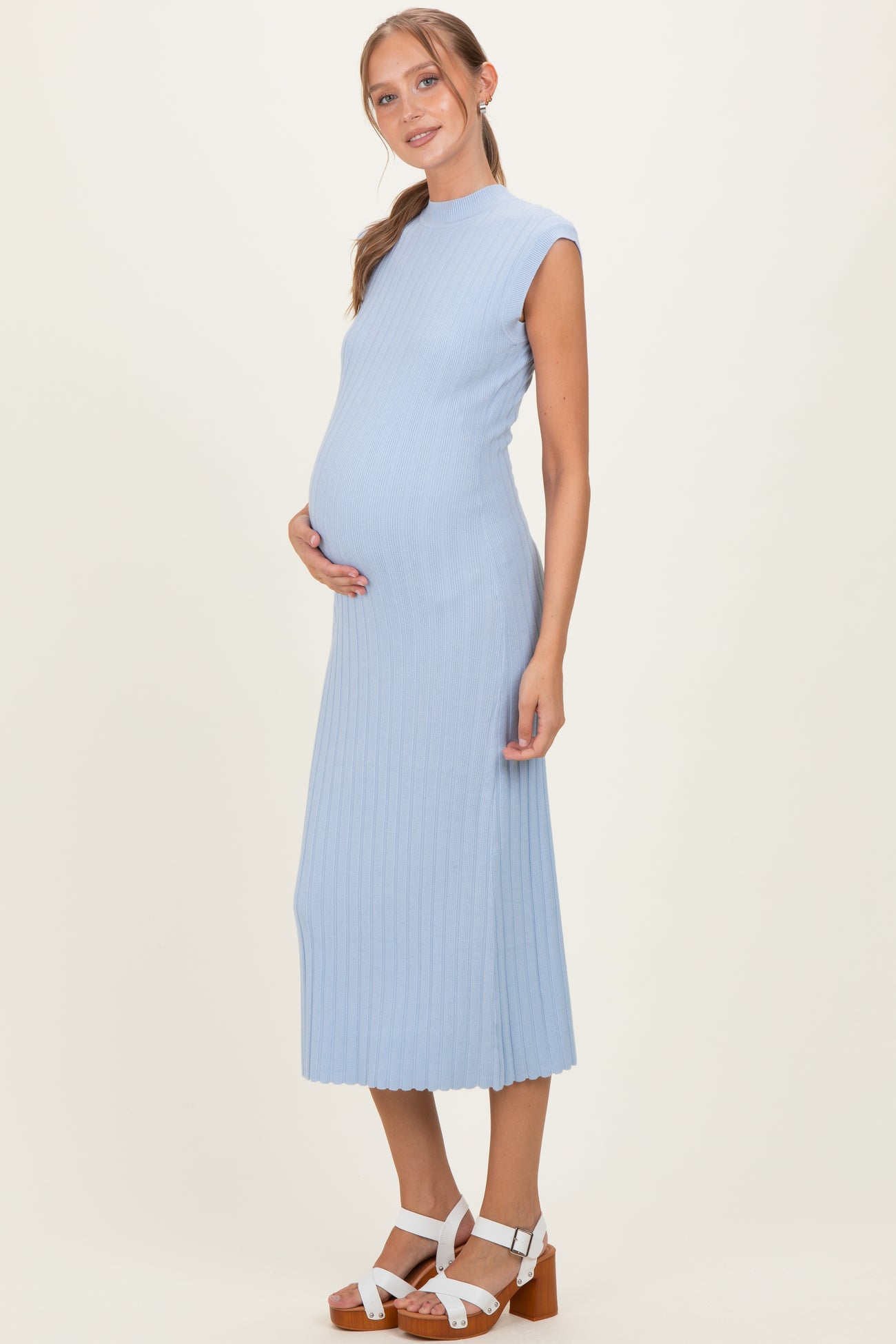 woman wearing a light blue ribbed maternity dress, showcasing her baby bump while standing with a neutral background