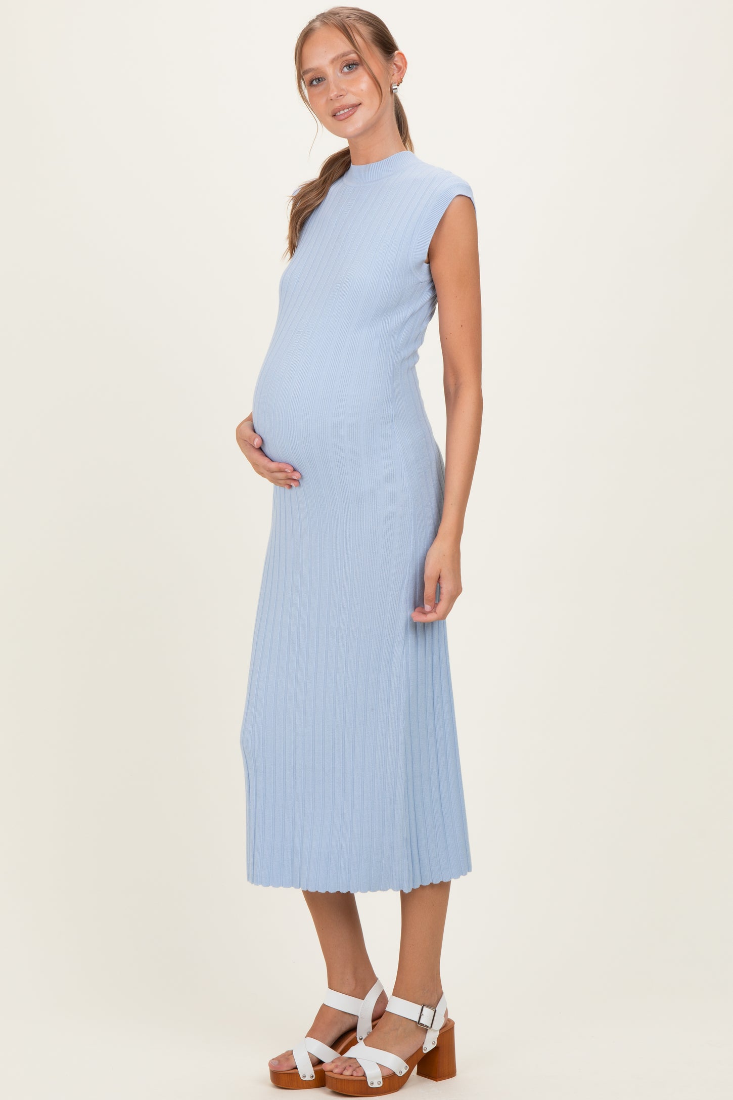 woman wearing a light blue ribbed maternity dress, showcasing her baby bump while standing with a neutral background