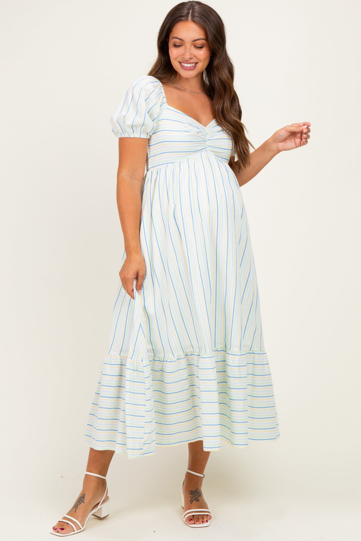 woman wearing a light blue and white striped maternity dress with puff sleeves and a tiered hem, showing her baby bump