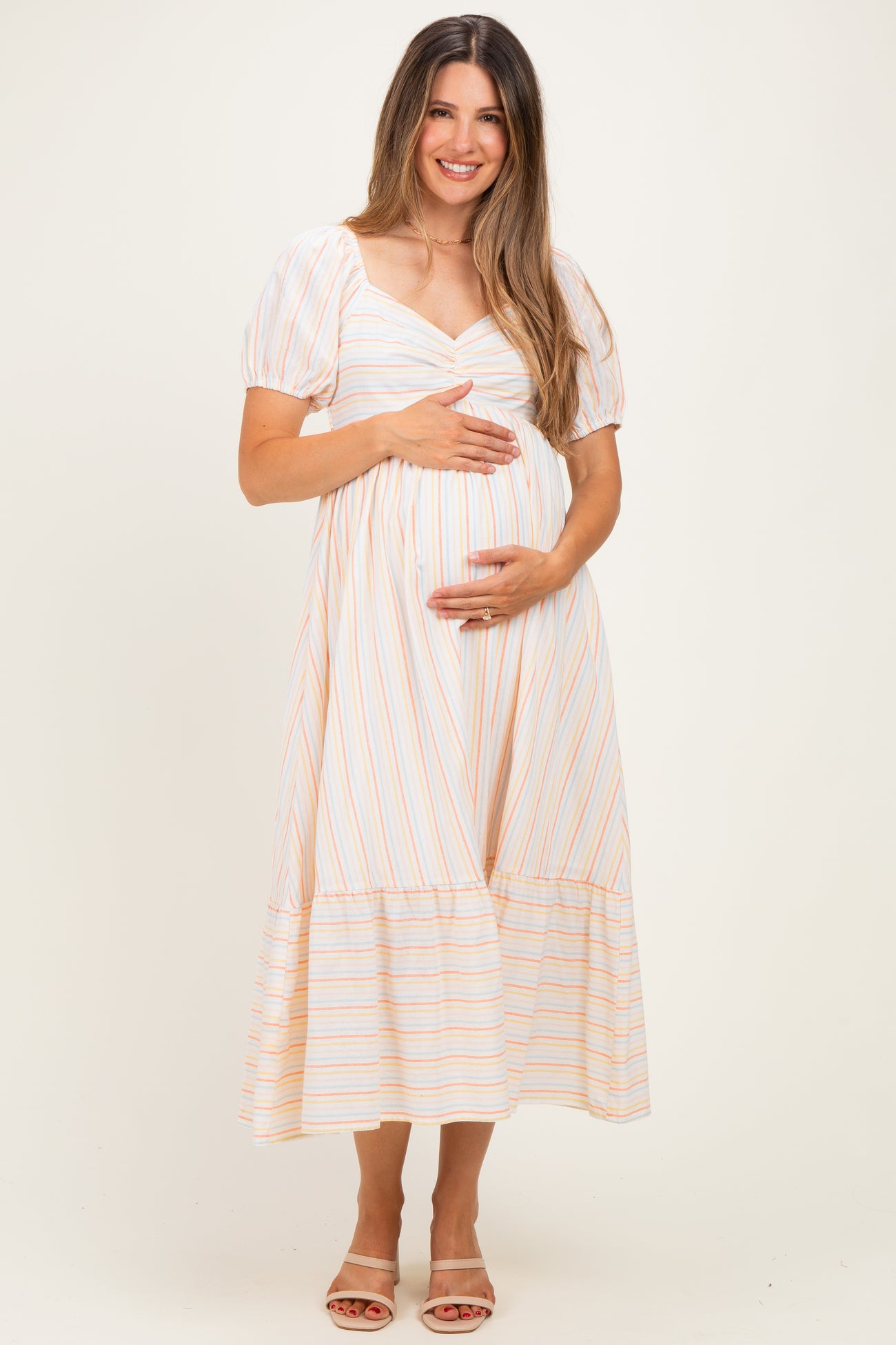 woman wearing a striped maternity dress with puff sleeves and a baby bump, standing and smiling