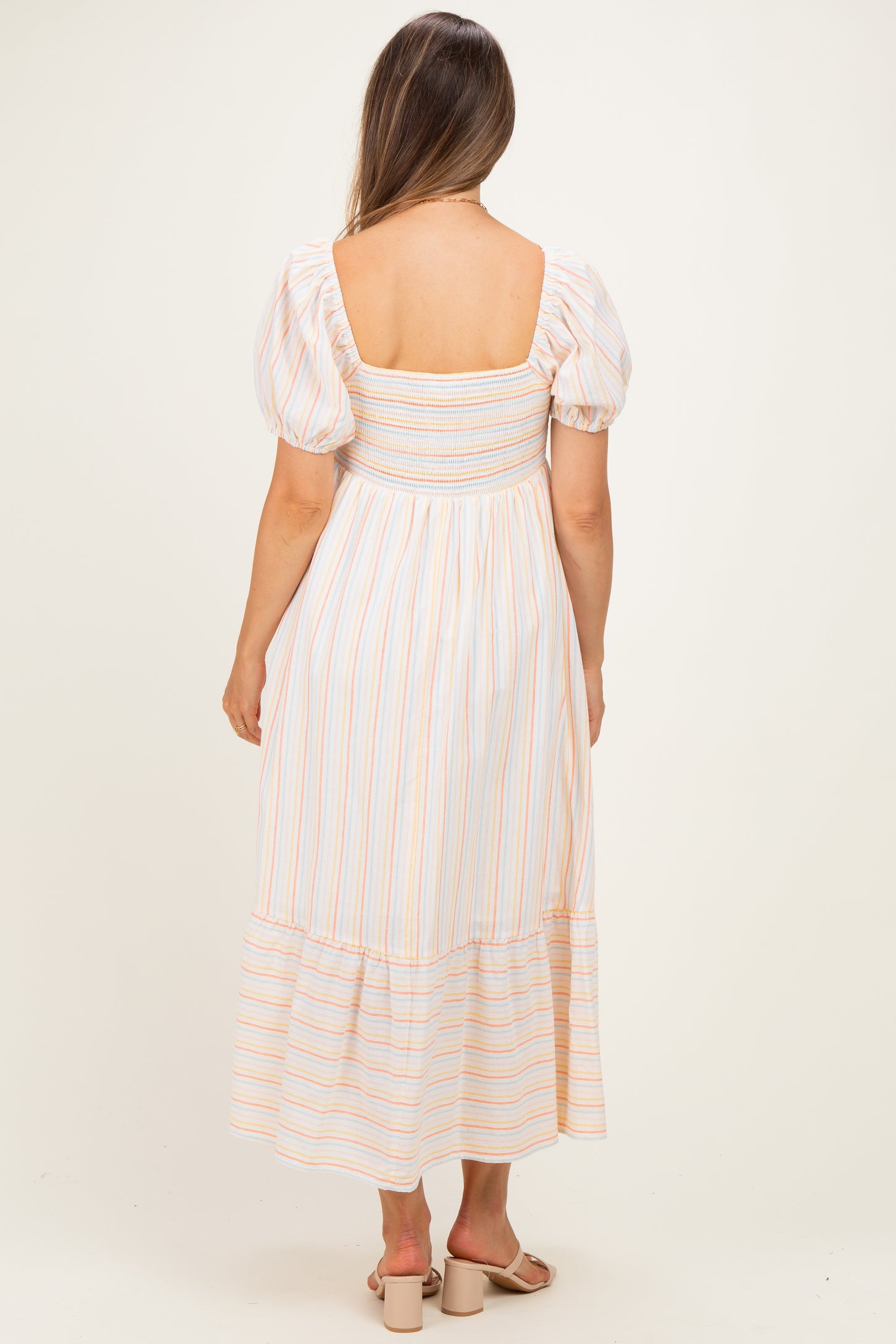 woman wearing a striped maternity maxi dress with puff sleeves and a smocked bodice, showing her back
