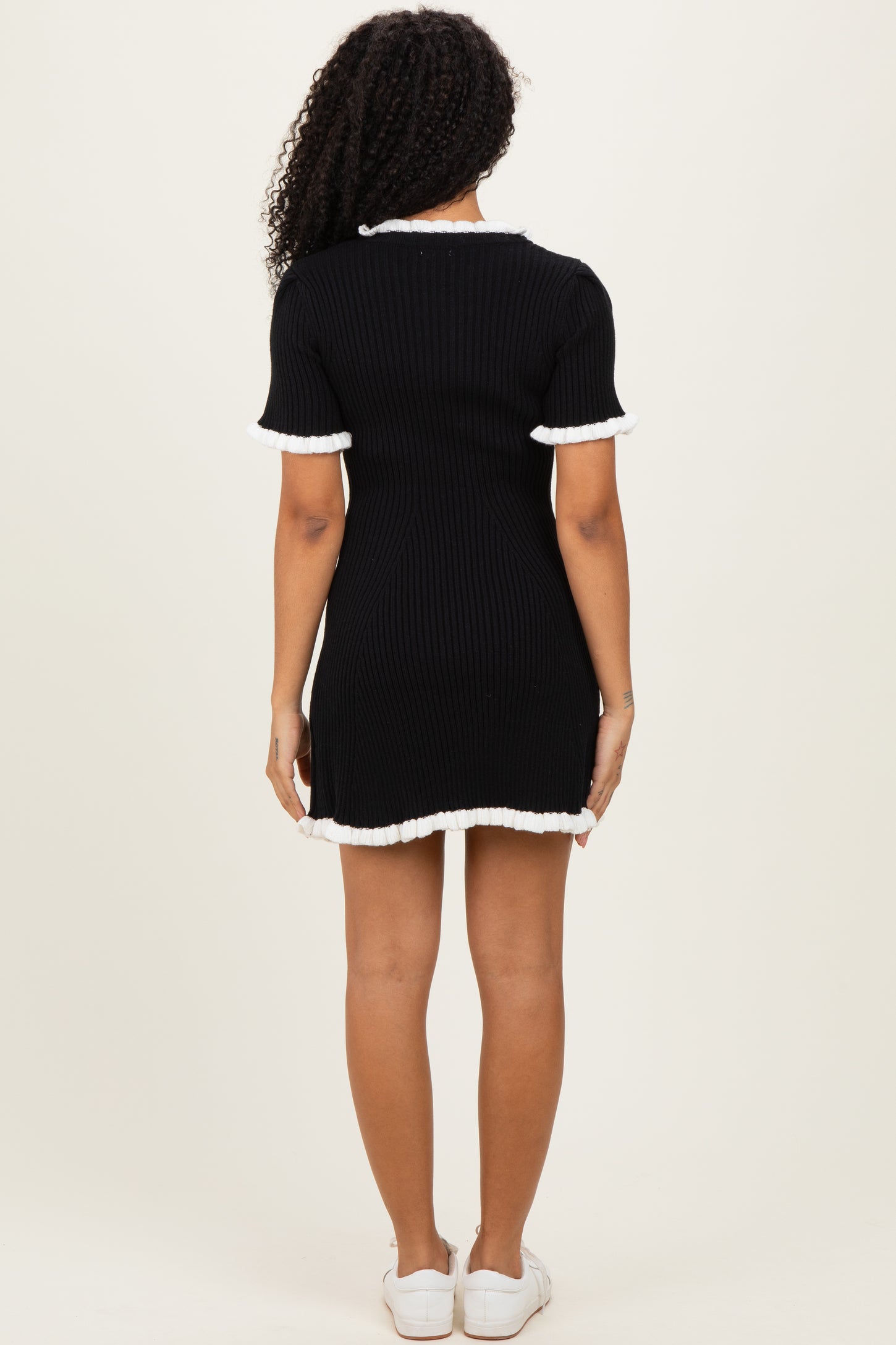 woman wearing a black ribbed short sleeve dress with white ruffled trim, shown from the back