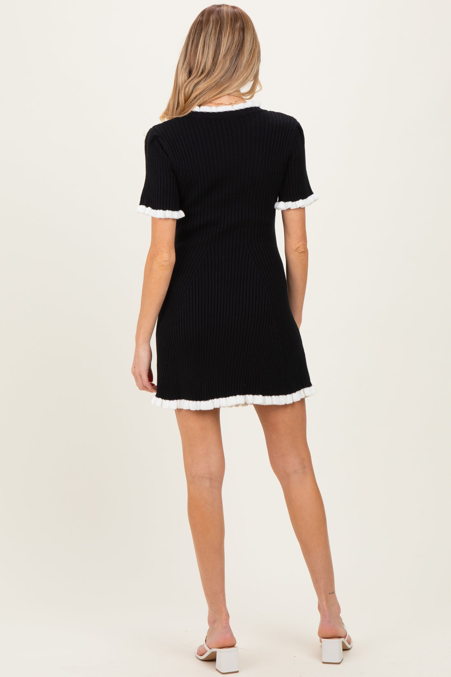 woman wearing a black ribbed maternity dress with white trimmed sleeves, showing the back view