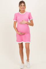 woman wearing a pink ribbed maternity dress with white ruffled sleeves and holding her baby bump
