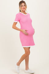 woman wearing a pink ribbed maternity dress with white trim, holding her baby bump