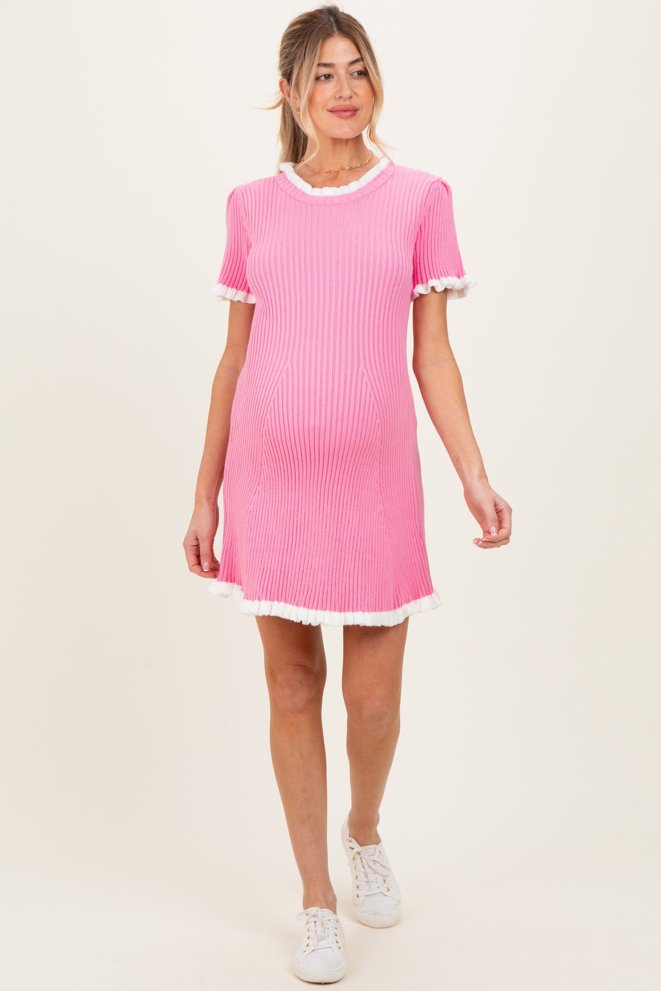 woman wearing a pink ribbed maternity dress with white ruffle details and a visible baby bump