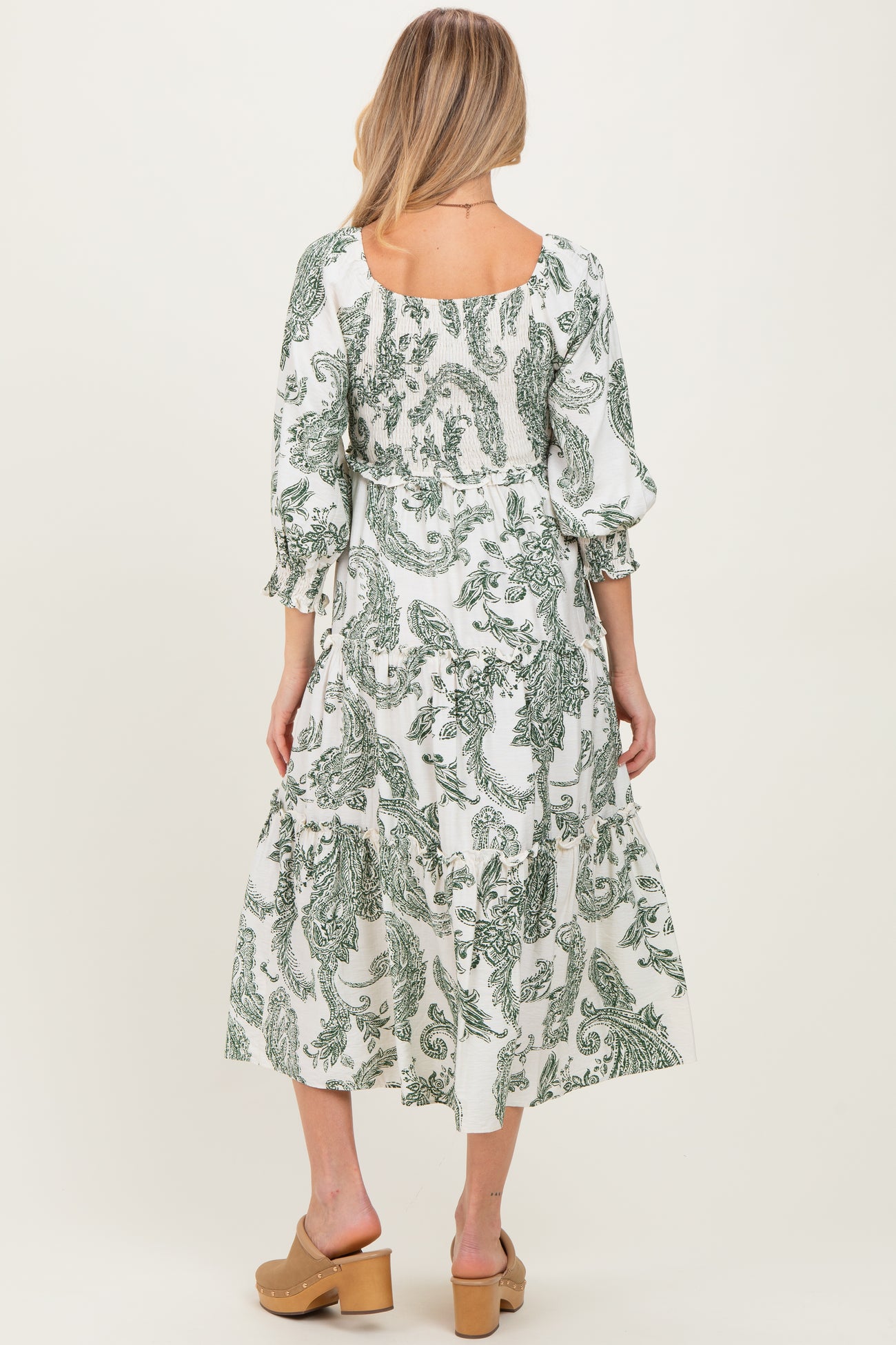 woman wearing a white maternity dress with green paisley print and puff sleeves, showing the back view