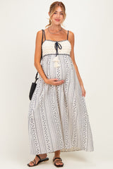 woman wearing a white patterned maternity maxi dress with a tie strap and holding her baby bump