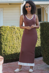 woman wearing a brown sleeveless maxi dress with a white trim at the neckline and hem, standing outdoors