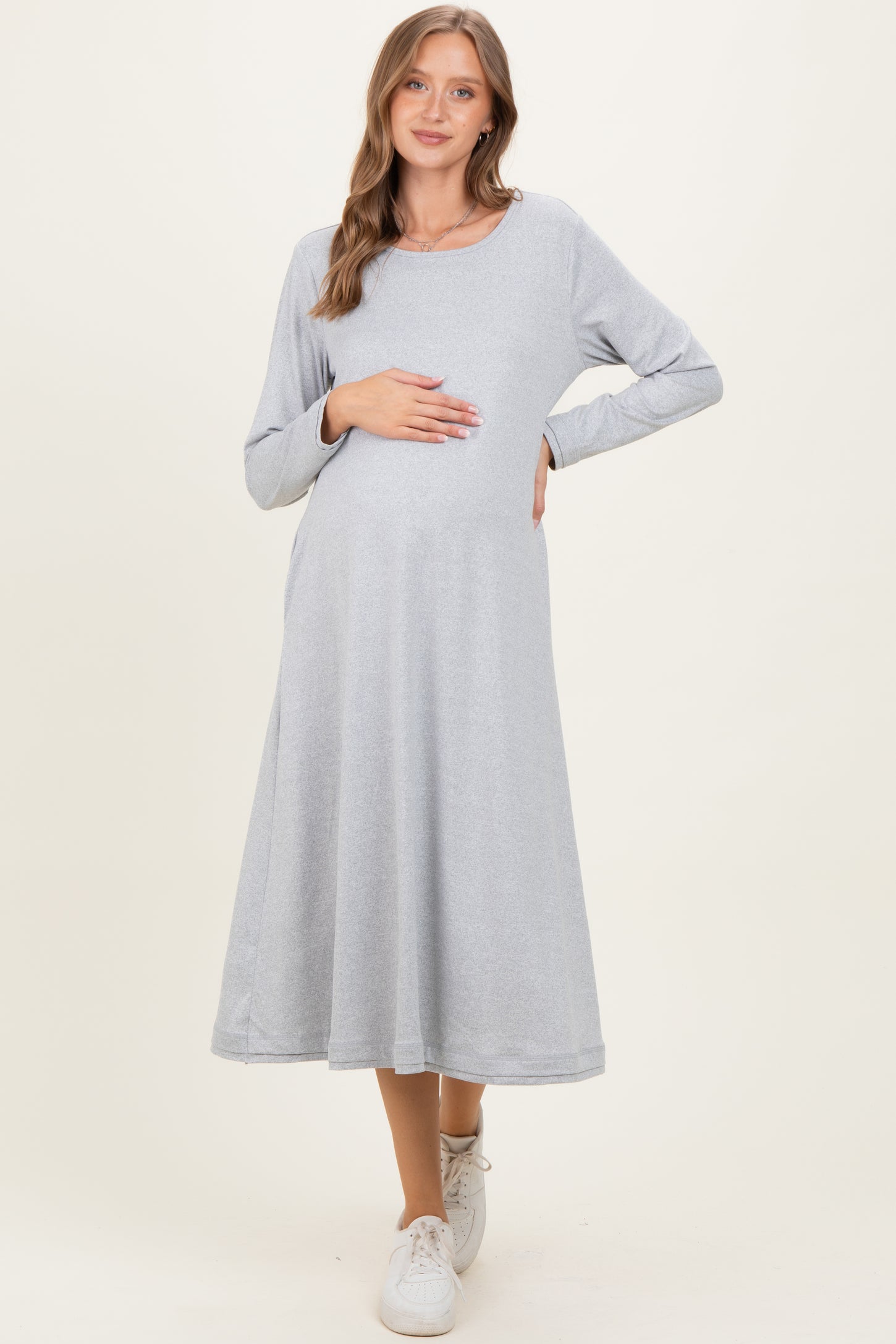 woman wearing a light grey long sleeve maternity dress and holding her baby bump