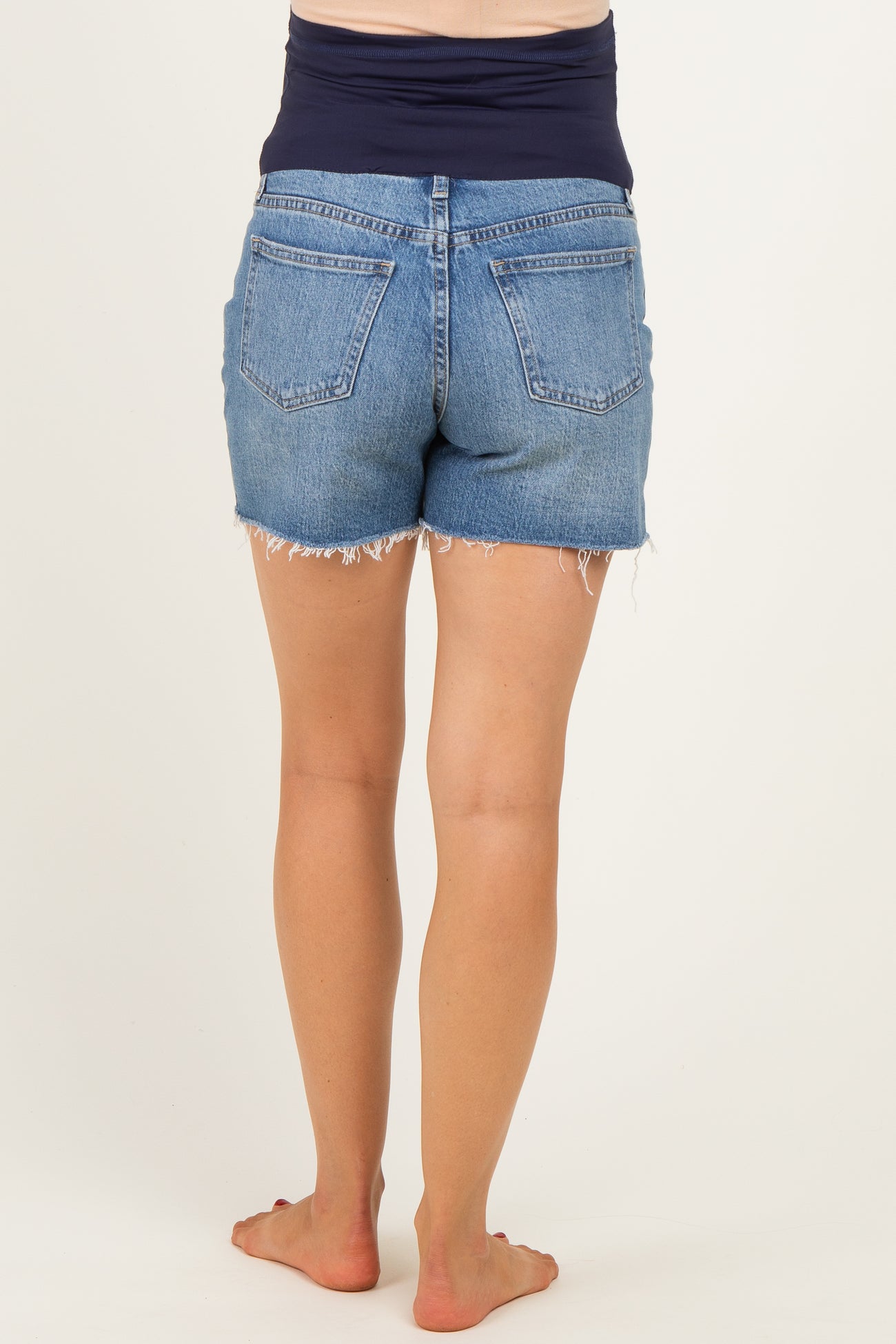 woman wearing maternity denim shorts with a frayed hem, showing the back view and no visible baby bump