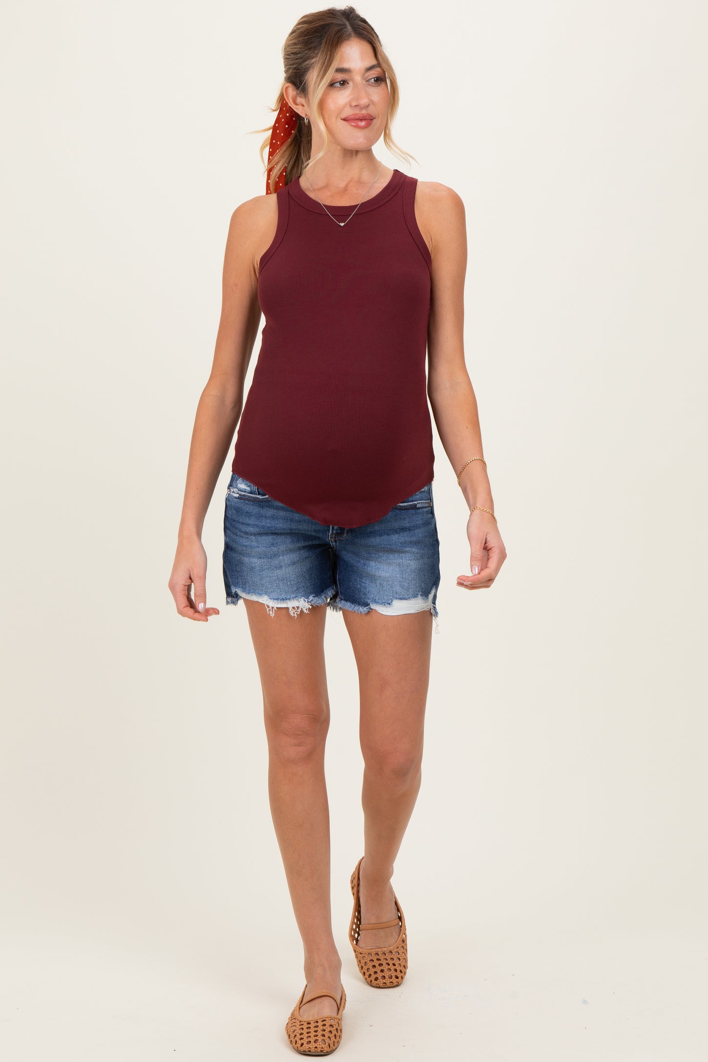 woman wearing a burgundy maternity tank top and denim shorts, showing her baby bump while walking
