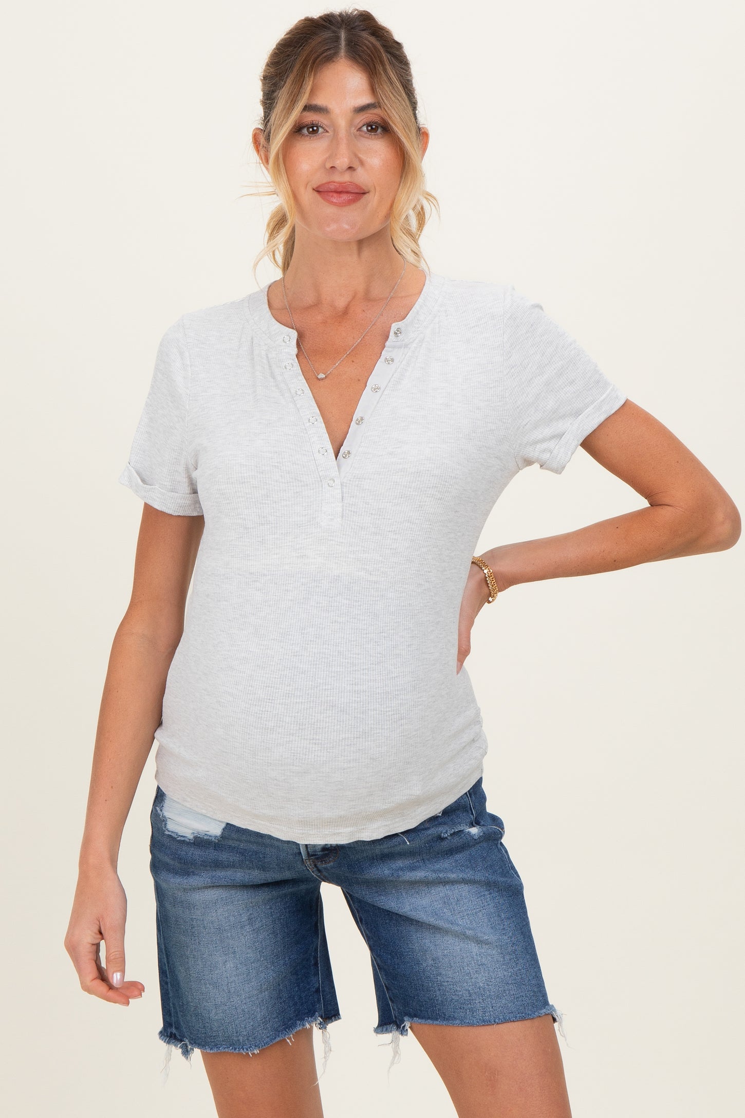 woman wearing a gray maternity short sleeve henley top and denim shorts, showing her baby bump