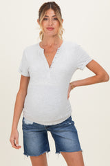 woman wearing a gray maternity short sleeve henley top and denim shorts, showing her baby bump