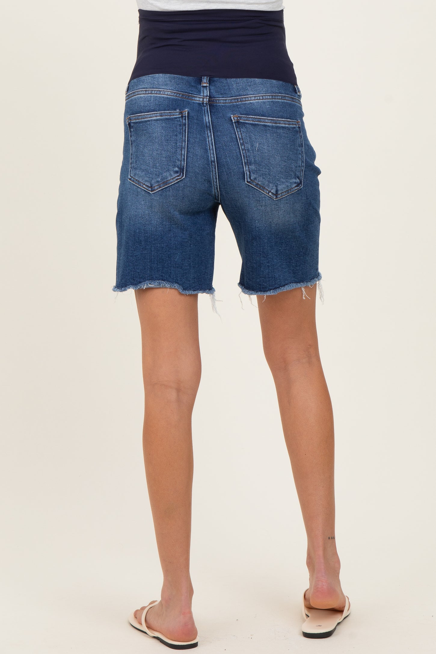 woman wearing dark wash maternity denim shorts with a stretchy waistband and frayed hem.