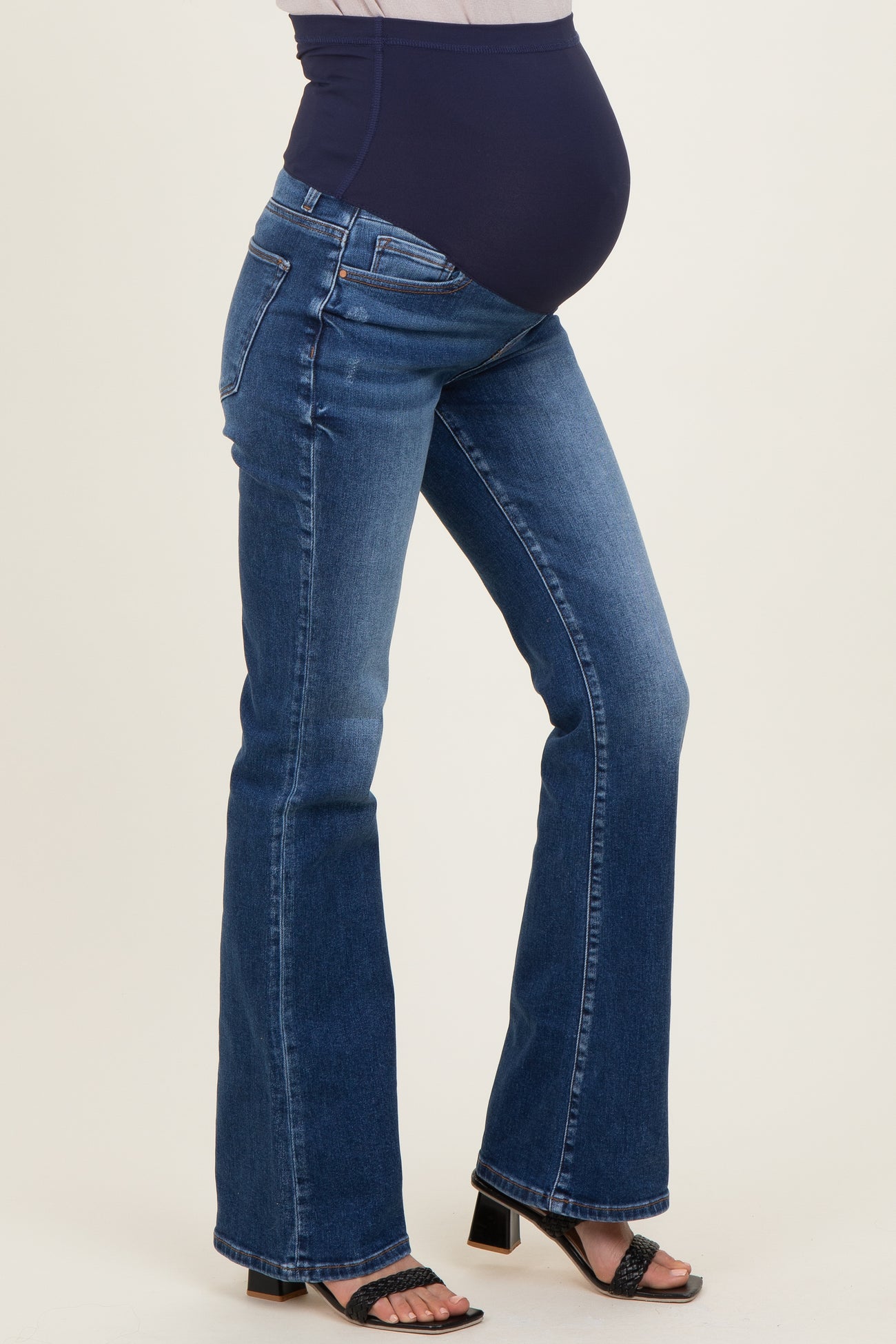 woman wearing dark blue maternity jeans with a wide waistband and flared legs, showing her baby bump