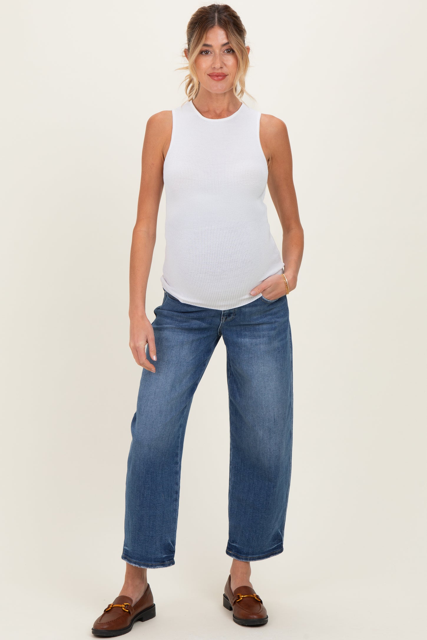 woman wearing a white sleeveless ribbed maternity top and blue wide-leg jeans, showing her baby bump