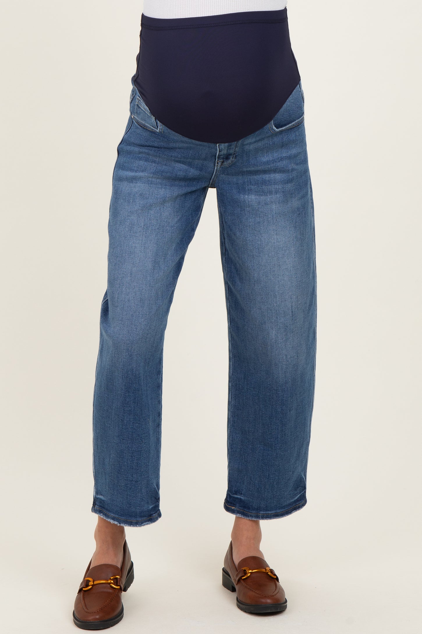 woman wearing blue maternity jeans with a dark waistband and cropped legs, standing in a neutral pose