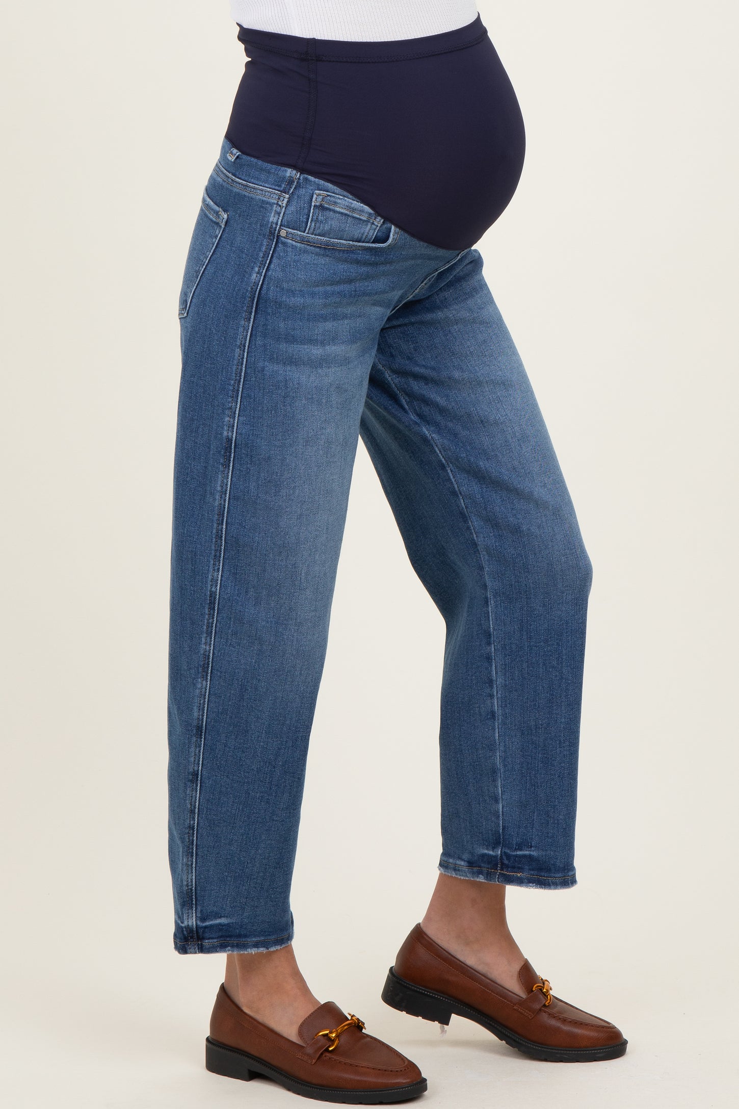 woman wearing a pair of blue maternity jeans with a black belly support panel and styled with brown loafers