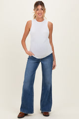 woman wearing a white sleeveless maternity top and blue wide-leg jeans, showing her baby bump