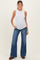 woman wearing a white sleeveless maternity top and blue wide-leg jeans, showing her baby bump