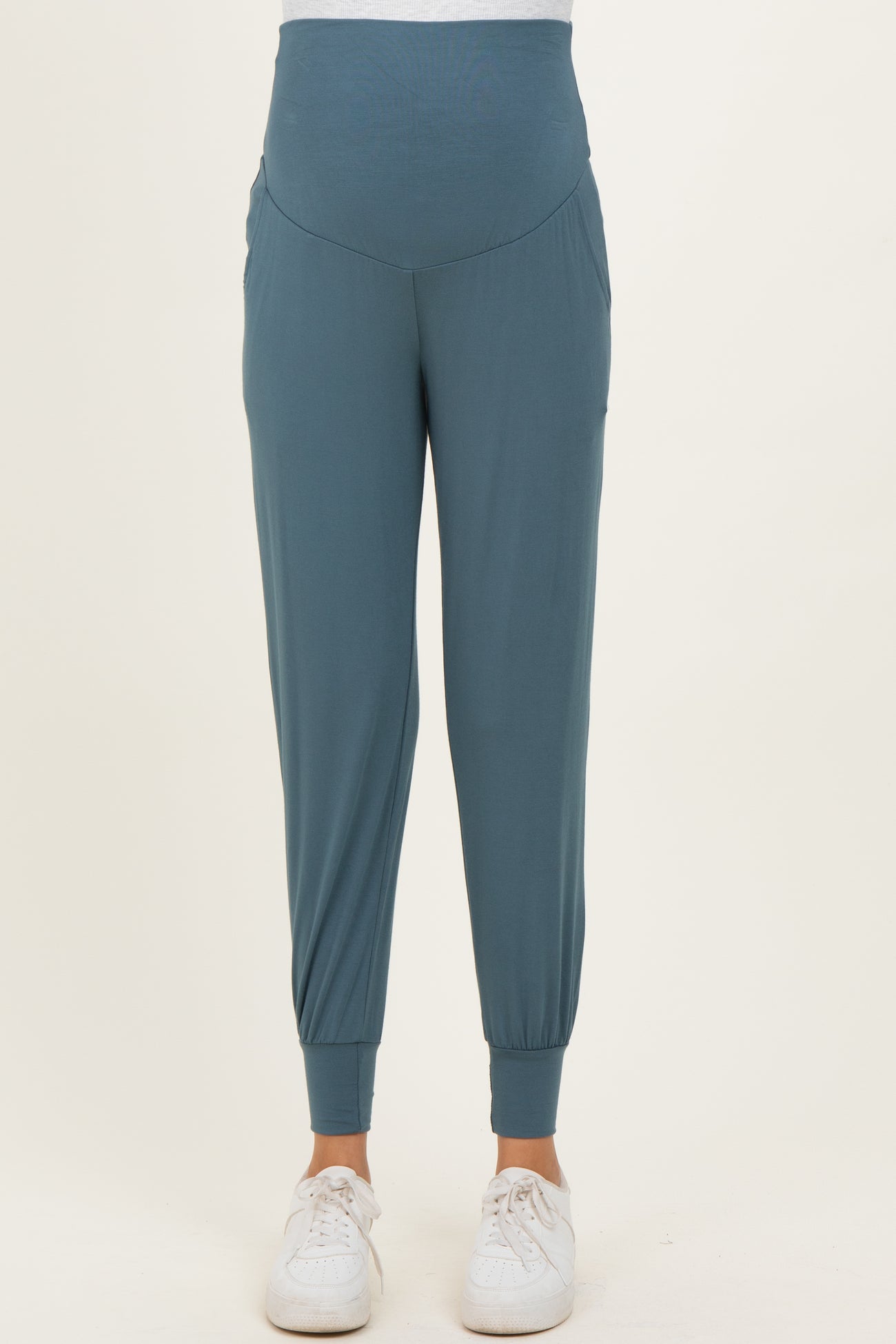 woman wearing teal maternity jogger pants with a high waistband and pockets, paired with white sneakers
