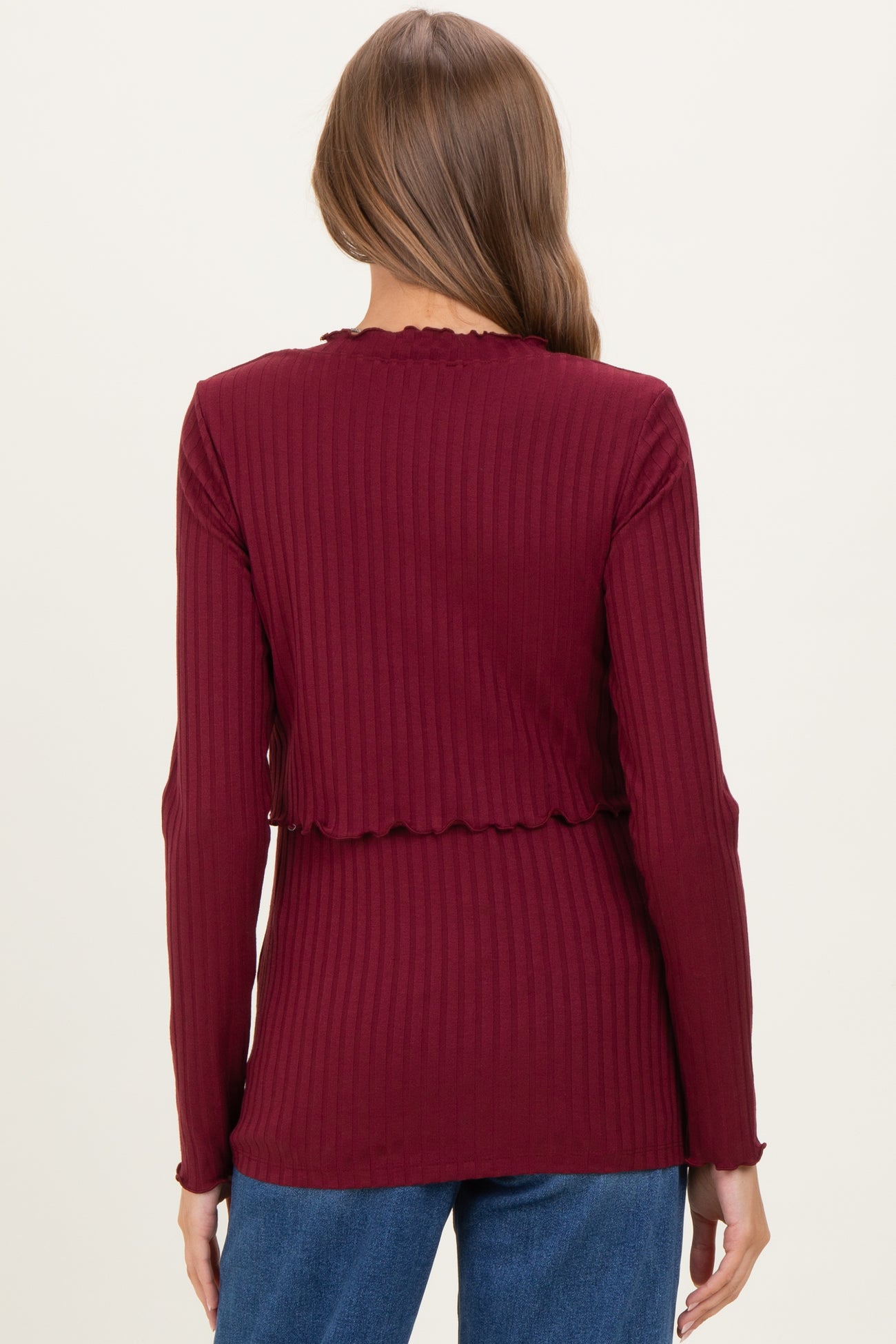 woman wearing a burgundy long sleeve maternity top with a ribbed texture and scalloped edges, shown from the back