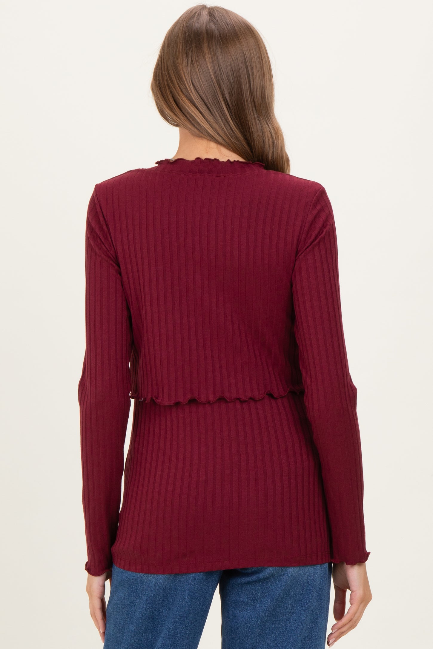 woman wearing a burgundy long sleeve maternity top with a ribbed texture and scalloped edges, shown from the back
