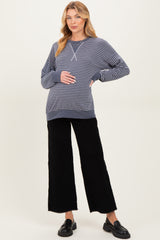 woman wearing a navy and white striped maternity sweatshirt and black wide-leg pants, softly cradling her baby bump