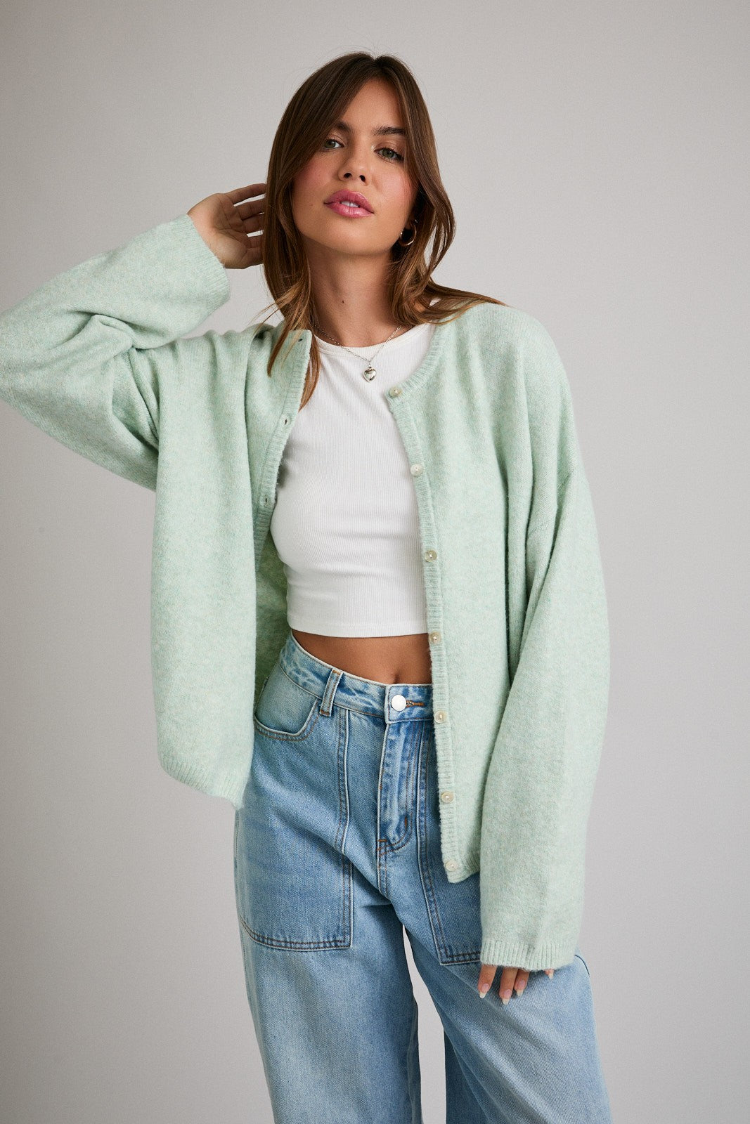 woman wearing a light green oversized cardigan over a white crop top and high-waisted blue jeans