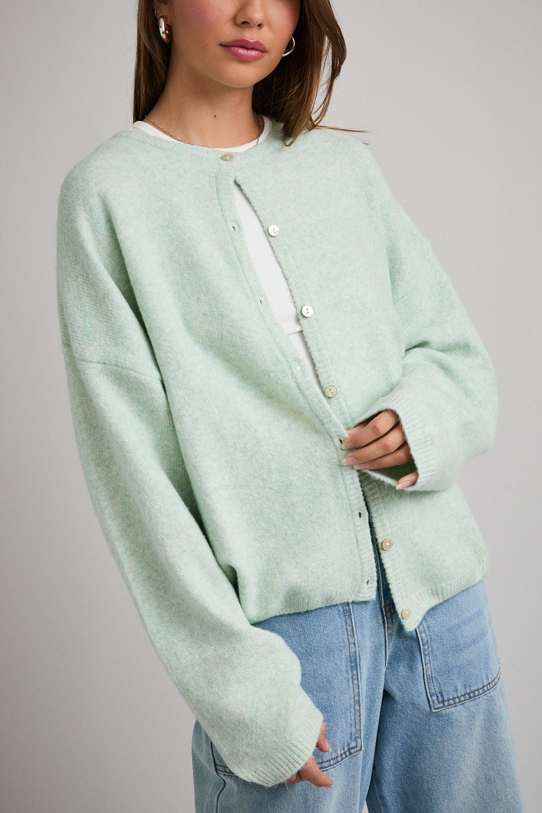 woman wearing a mint green oversized cardigan with buttons styled over a white top and light blue jeans