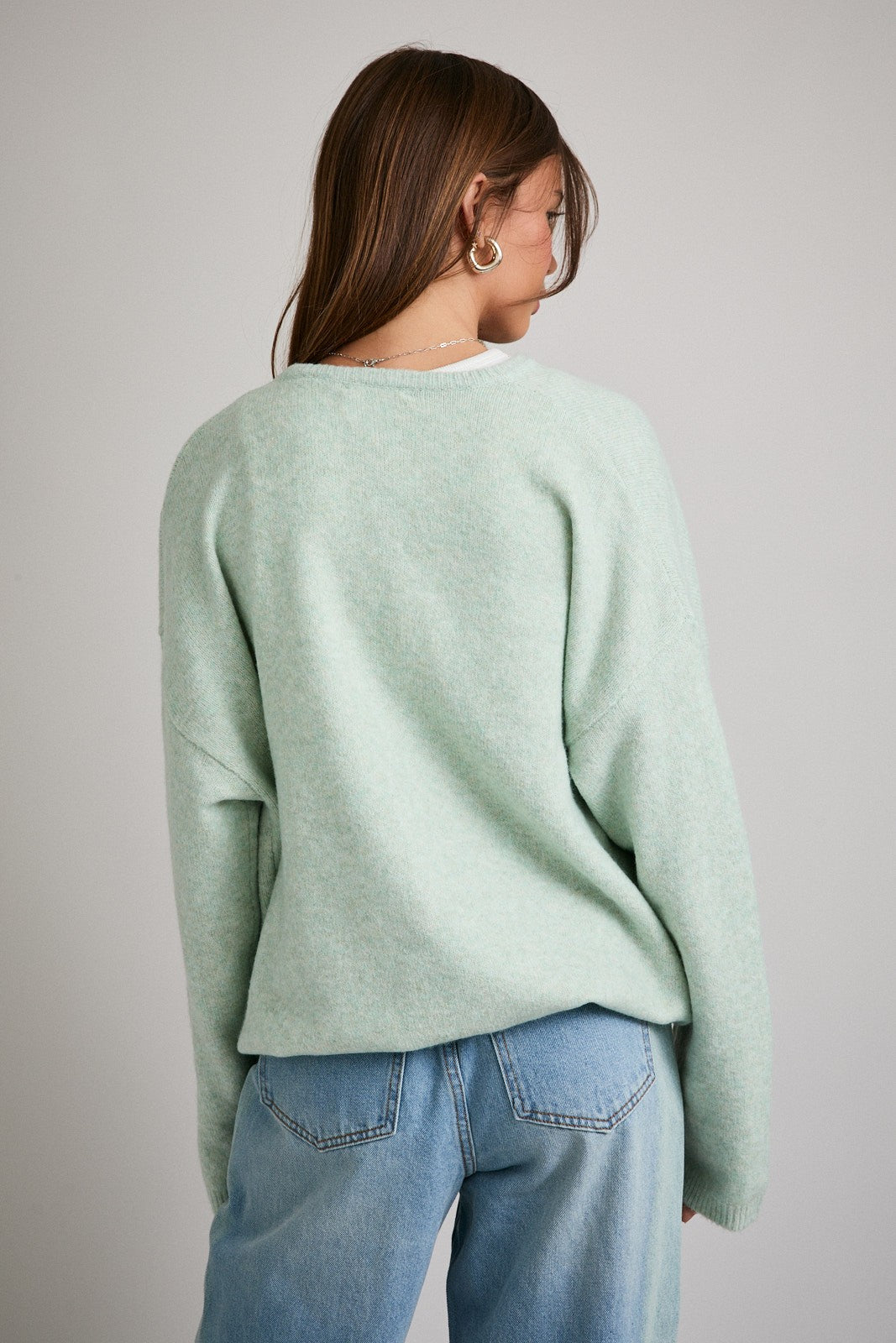 woman wearing a soft mint green oversized sweater with a relaxed fit and back view, paired with light blue jeans
