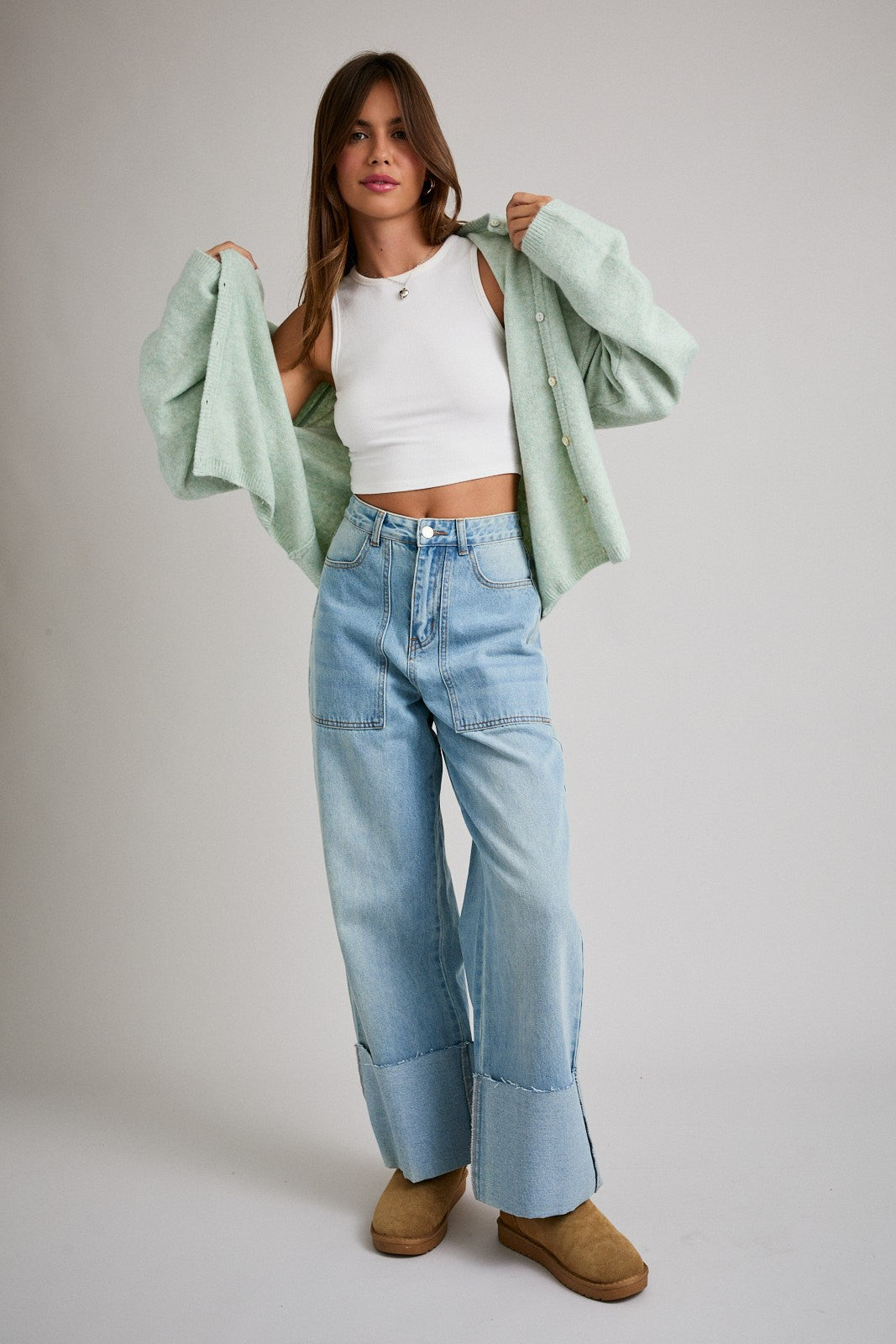 woman wearing a white cropped tank top, mint green button-up cardigan, and light blue wide-leg jeans with tan slippers